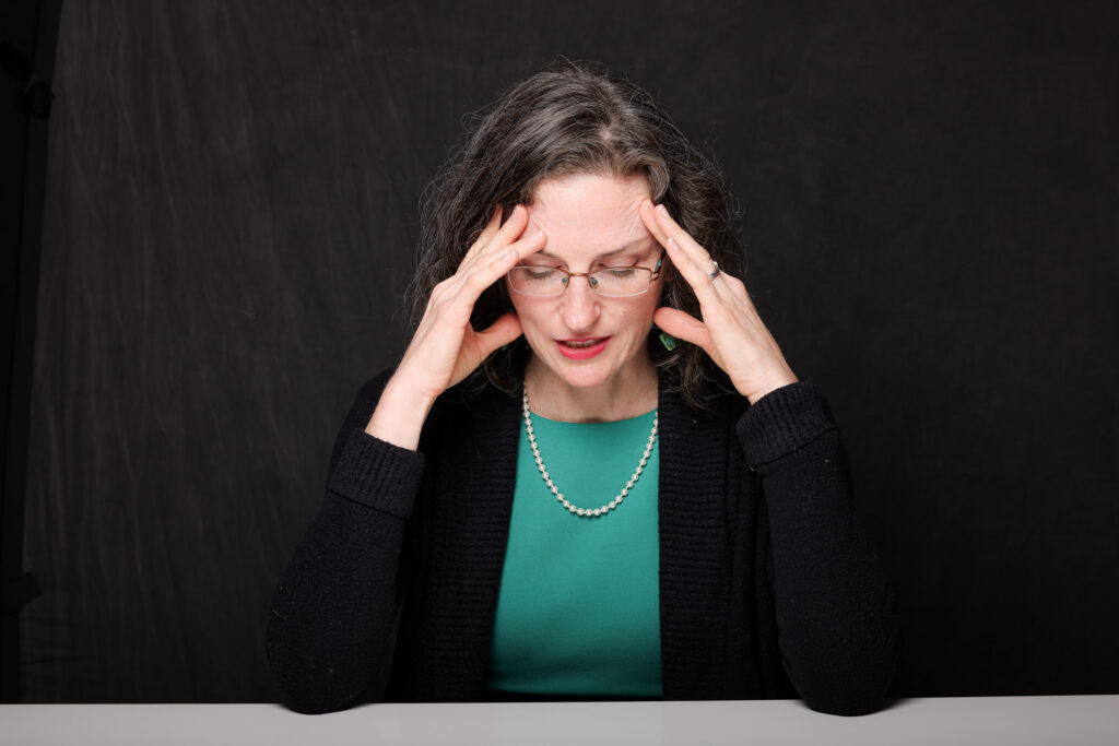 Woman with brown hair hands on face contemplating situation