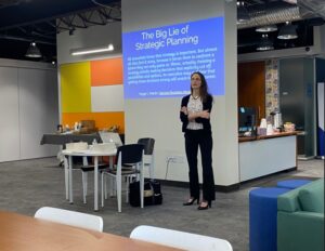 Nettie Owens standing professionally at front of event space ready to present on strategic planning with sparse attendance and empty chairs